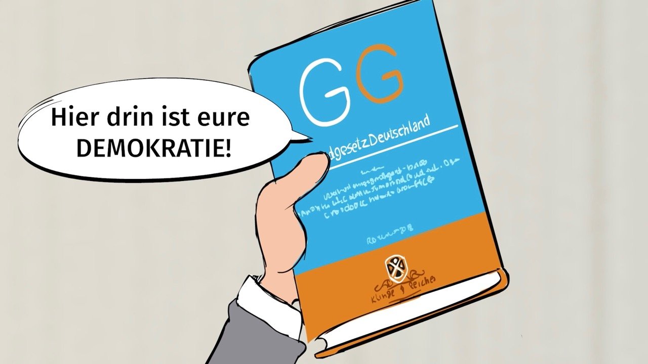 Das Bild zeigt eine Grafik, auf der eine Hand eine Ausgabe des Grundgesetzes hochhält. Neben dem Grundgesetz ist eine Sprechblase, in der steht: "Hier drin ist eure Demokratie!".