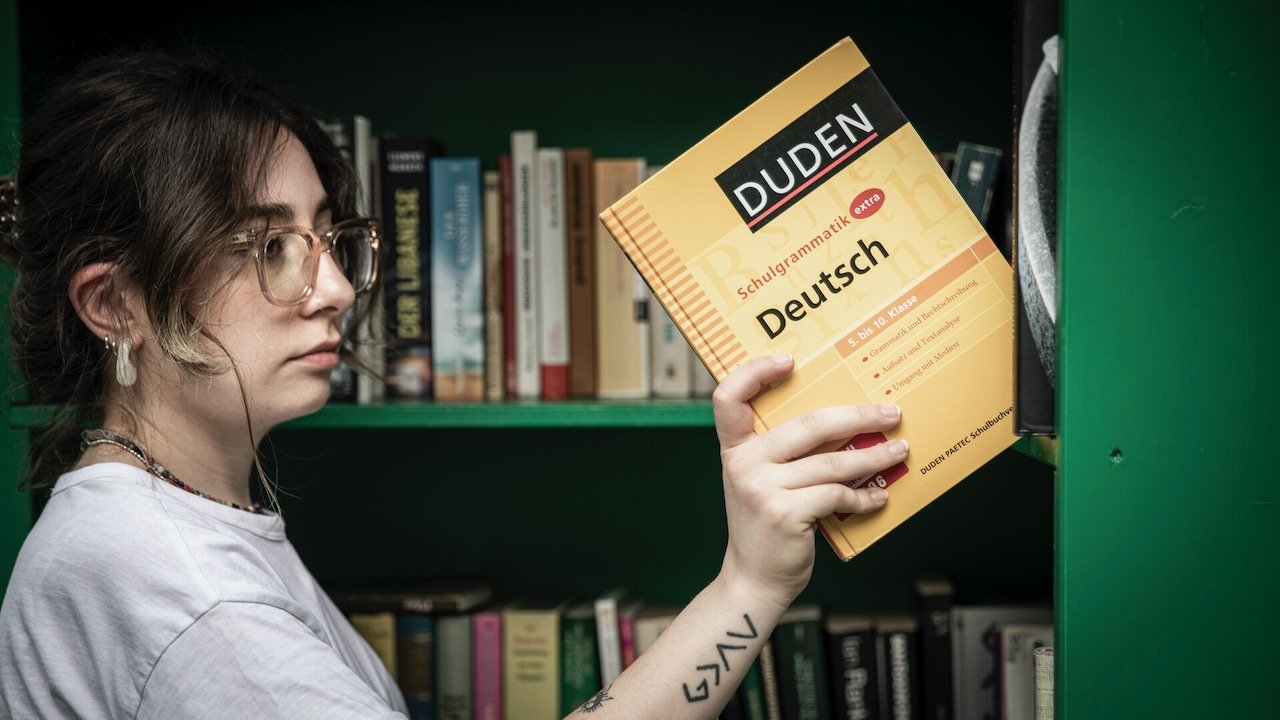 Young women placing a German grammar book on a bookshelf