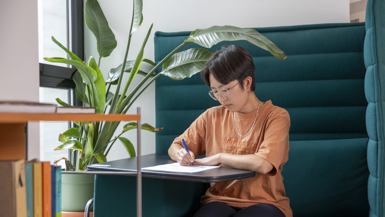 Person sitzt an einem Tisch und füllt Formular aus.