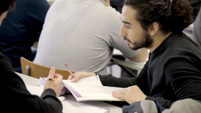 Das Bild zeigt einen jungen Mann in einem vollen Seminarraum. 